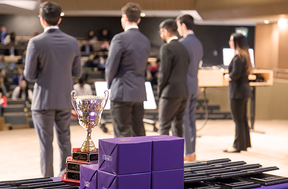 Close-up of BDO Venture trophy, four students' backs facing the trophy