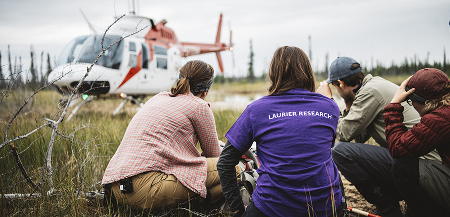 Researchers crouched in front of helicopter