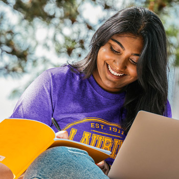 female student wearing purple Laurier t-shirt smiling at yellow notebook